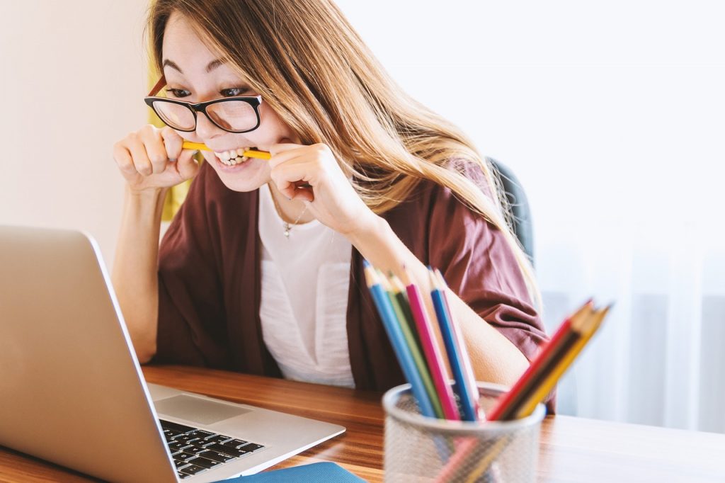 Woman looking at laptop computer and biting a pencil.